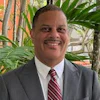 Professional headshot of man in gray suit and burgundy striped tie smiling at camera