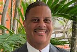 Professional headshot of man in gray suit and burgundy striped tie smiling at camera