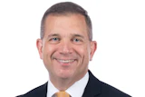 Professional headshot of a smiling man in business attire with dark suit and gold tie