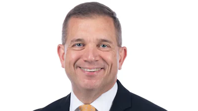 Professional headshot of a smiling man in business attire with dark suit and gold tie