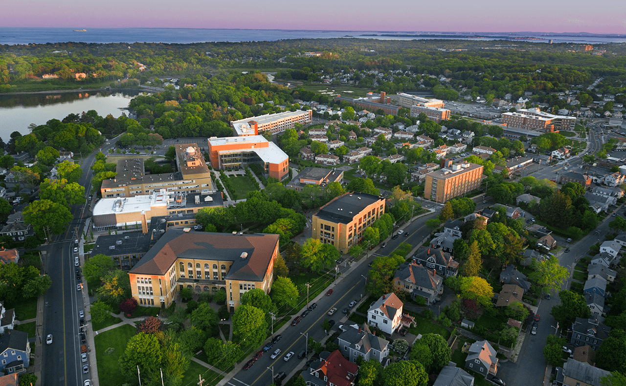 Aerial view of suburban community with orange institutional buildings, residential homes, tree-lined streets, and river at dusk
