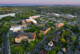 Aerial view of suburban community with orange institutional buildings, residential homes, tree-lined streets, and river at dusk
