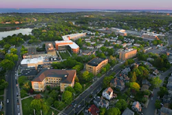 Aerial view of suburban community with orange institutional buildings, residential homes, tree-lined streets, and river at dusk