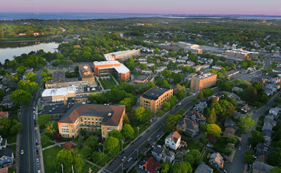 Aerial view of suburban community with orange institutional buildings, residential homes, tree-lined streets, and river at dusk