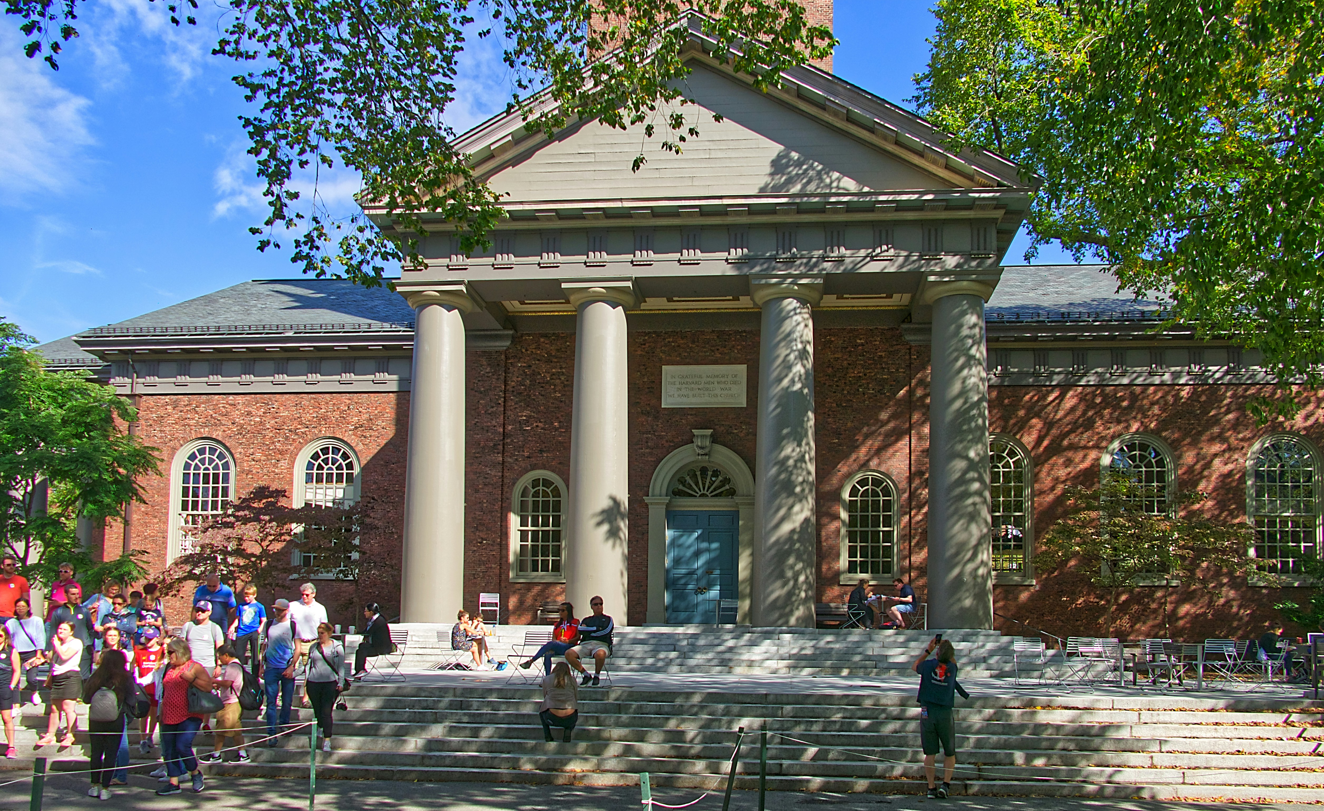 Historic brick building with classical columns and portico, surrounded by visitors on a sunny day