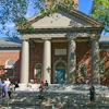 Historic brick building with classical columns and portico, surrounded by visitors on a sunny day