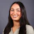 Professional headshot of a smiling woman with long dark hair wearing a light gray ribbed sweater and delicate necklace against a gray background