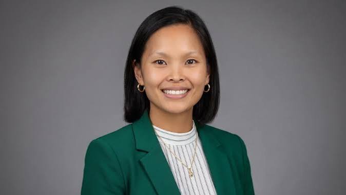 Professional headshot of a smiling woman wearing a green blazer and white striped shirt