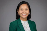 Professional headshot of a smiling woman wearing a green blazer and white striped shirt