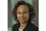 Professional headshot of a woman in business attire with checkered blouse and dark blazer