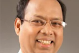 Professional headshot of a smiling man wearing glasses and light-colored shirt