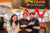 Three Stanford students holding plates of Asian noodle dishes at Star Ginger restaurant with festive red decorations