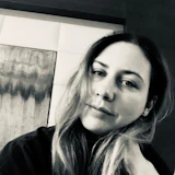 Black and white portrait of a woman with long hair wearing dark clothing, looking at camera indoors