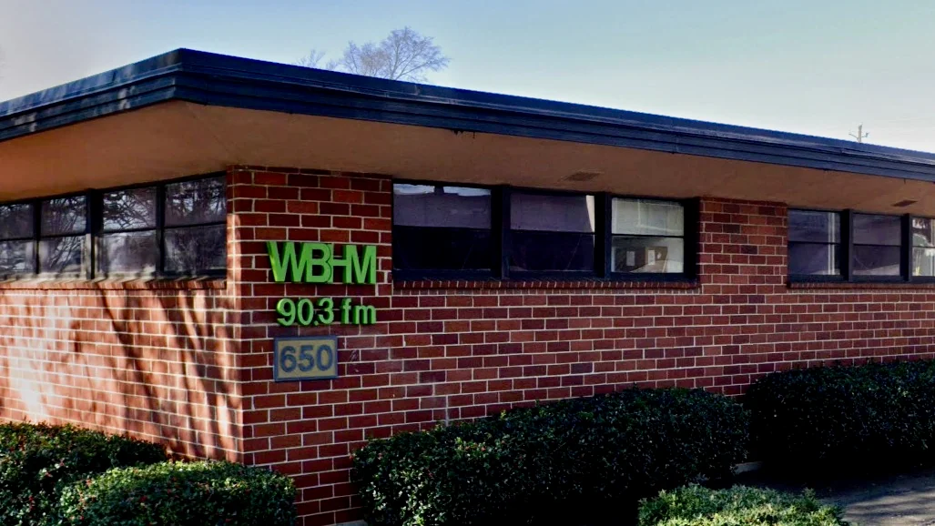 WBAV 903 FM radio station signage on brick building exterior with windows and hedges