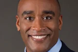 Professional headshot of a smiling man in business attire with blue shirt and tie