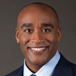 Professional headshot of a smiling man in business attire with blue shirt and tie